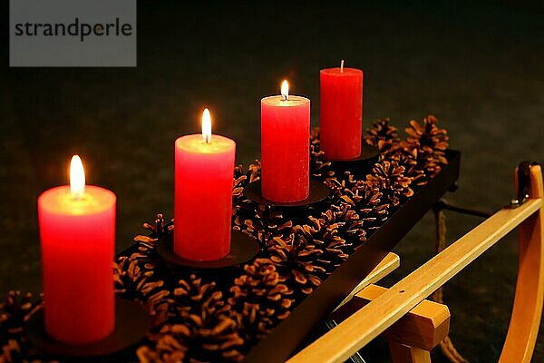 Vier Adventskerzen dekoriert mit Tannenzapfen auf einem Schlitten  Dritter Advent drei Kerzen brennen