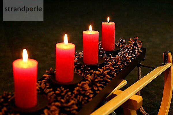 Vier Adventskerzen dekoriert mit Tannenzapfen auf einem Schlitten  Vierter Advent vier Kerzen brennen