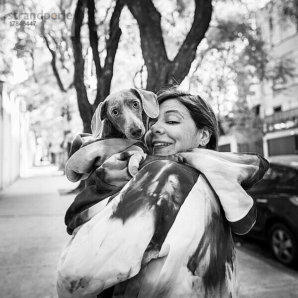 Lateinamerikanische Frau hält ihren Hund. Beide sind gleich gekleidet und schauen in die Kamera