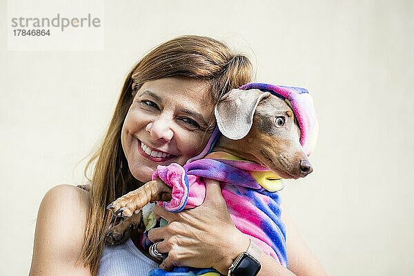 Lateinamerikanische Frau hält ihren Hund  beide gleich gekleidet. Sie schaut in die Kamera