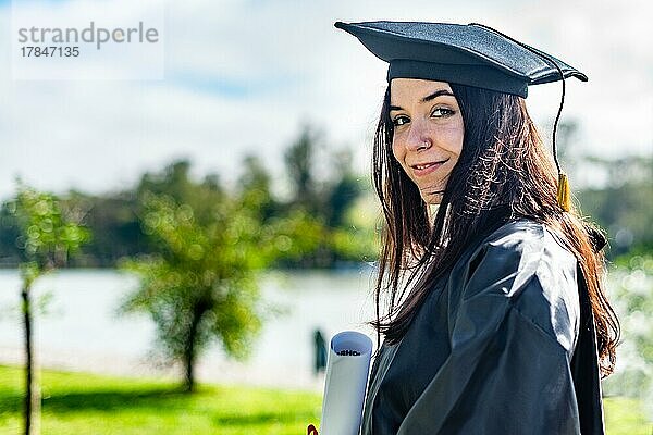 Glückliches kaukasisches Mädchen mit langem braunem Haar  das ein Diplom hält und in die Kamera schaut