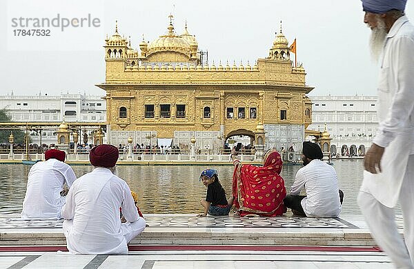 Indische Frau  Mädchen und Männer in weißen Anzügen sitzen am Rand des Wasserbeckens des Amrit Sagar oder Heiliger See  am Hari Mandir oder Goldener Tempel  Amritsar  Punjab  Indien  Asien