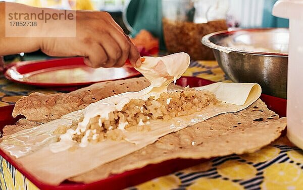 Hände machen nicaraguanischen Quesillo. Mittelamerikanisches Essen der Quesillo  Blick auf den traditionellen Quesillo mit eingelegten Zwiebeln  Zubereitung des traditionellen nicaraguanischen Quesillo