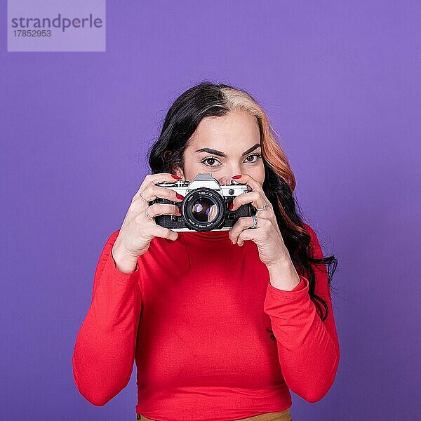 Attraktive junge Frau  die ein Foto mit ihrer Filmkamera vor einem violetten Hintergrund macht
