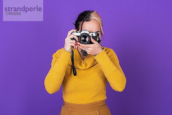 Attraktive junge Frau  die ein Foto mit ihrer Filmkamera vor einem violetten Hintergrund macht