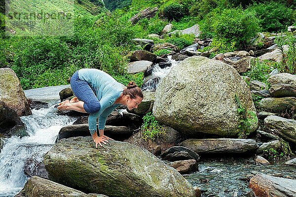 Frau macht Kakasana asana  Krähenpose Arm Balance im Freien an tropischen Wasserfall