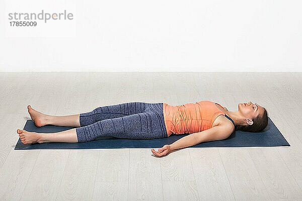 Schöne sportliche fit Yogini Frau entspannt in Yoga Asana Savasana  Körperhaltung im Studio