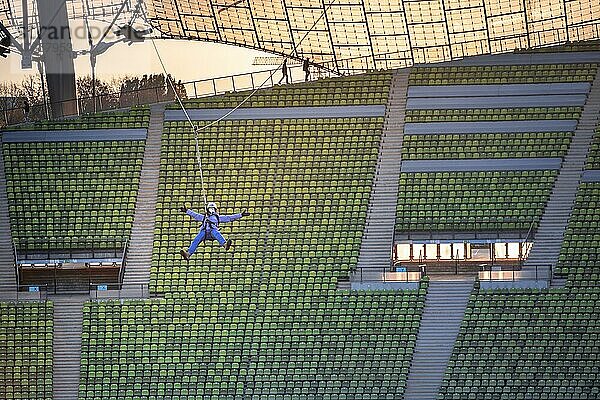 Frau schwingt an einer Zip-Line über dem Olympiastadion  Olympiastadion mit Zeltdach bei Sonnenuntergang  Olympiapark  München  Bayern  Deutschland  Europa