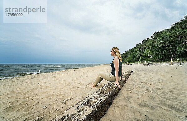 Glückliche Frau sitzt auf einem Holzbalken an einem einsamen Stand  Baltische See. Pole