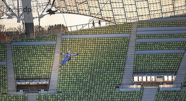 Frau schwingt an einer Zip-Line über dem Olympiastadion  Olympiastadion mit Zeltdach bei Sonnenuntergang  Olympiapark  München  Bayern  Deutschland  Europa