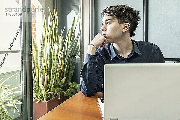 Junger nachdenklicher Mann im Büro mit Blick durch das Fenster