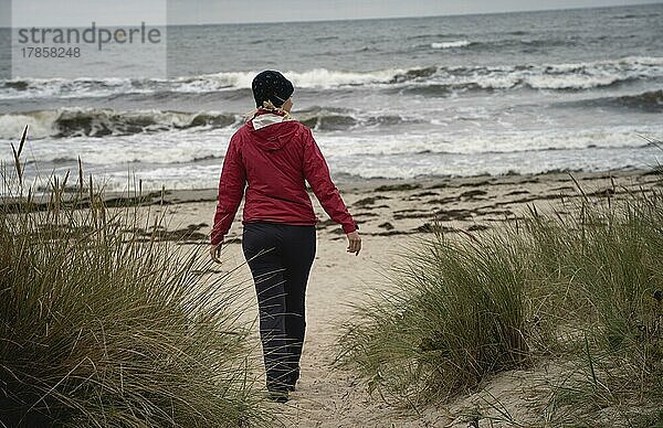 Frau in rot läuft an Sandstrand an der Ostsee bei düsterem Wetter  Insel Rügen  Deutschland  Europa