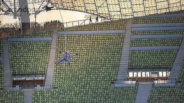 Frau schwingt an einer Zip-Line über dem Olympiastadion  Olympiastadion mit Zeltdach bei Sonnenuntergang  Olympiapark  München  Bayern  Deutschland  Europa