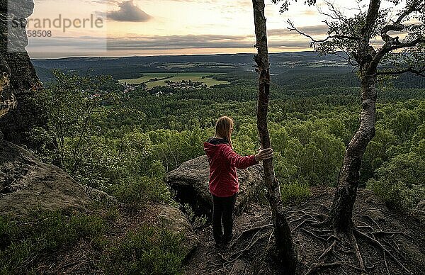 Frau in rot steht auf der Spitze einer Gebirgskette im Elbsandsteingebirge und beobachtet den Sonnenaufgang  Elbsandsteingebirge  Dresden  Deutschland  Europa