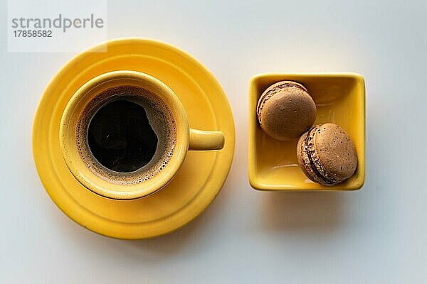 Top Winkel einer gelben Tasse schwarzen Kaffee und zwei Makronen auf weißem Hintergrund