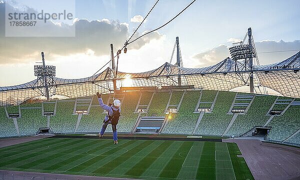 Frau schwingt an einer Zip-Line über dem Olympiastadion  Olympiastadion mit Zeltdach bei Sonnenuntergang  Olympiapark  München  Bayern  Deutschland  Europa