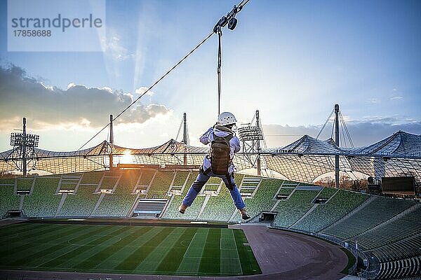 Frau an einer Zip-Line über dem Olympiastadion  Olympiastadion mit Zeltdach bei Sonnenuntergang  Olympiapark  München  Bayern  Deutschland  Europa