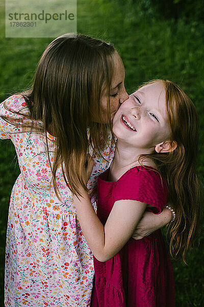 Die große Schwester küsst und umarmt die kleine Schwester  während sie lächelt und lacht