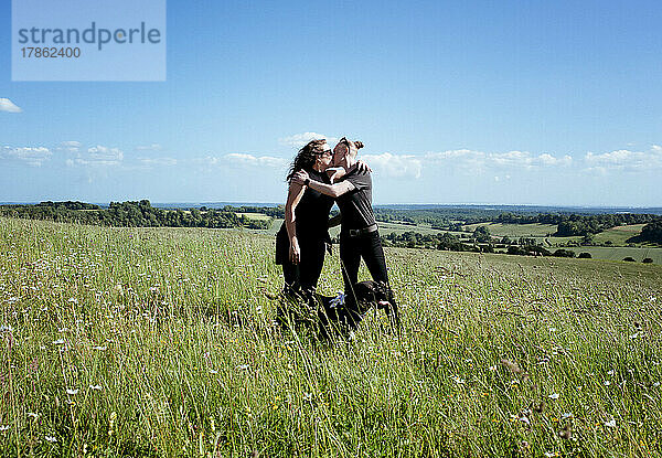 Lesbisches Paar küsst sich auf einem Feld mit seinem Hund auf dem Land