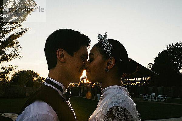 Multiracial bride and groom snuggle and kiss in backlight