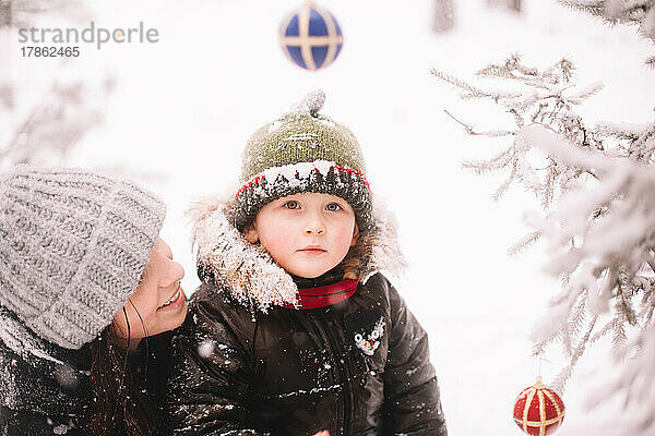 Porträt einer glücklichen Mutter und ihres Sohnes am Weihnachtsbaum im Freien im Winter