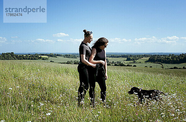 Lesbisches Paar umarmt sich  während es mit seinem Hund auf dem Land spazieren geht