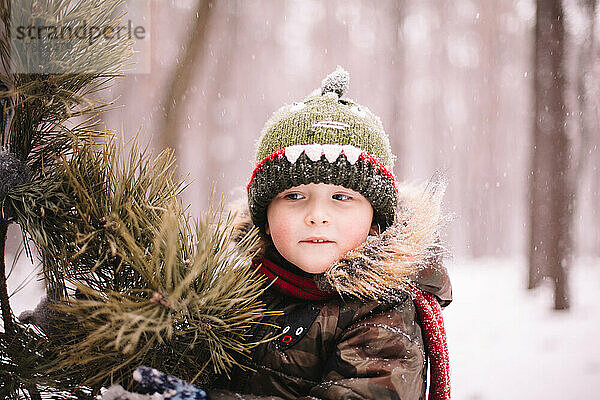 Nachdenklicher kleiner Junge steht im Winter draußen am Weihnachtsbaum