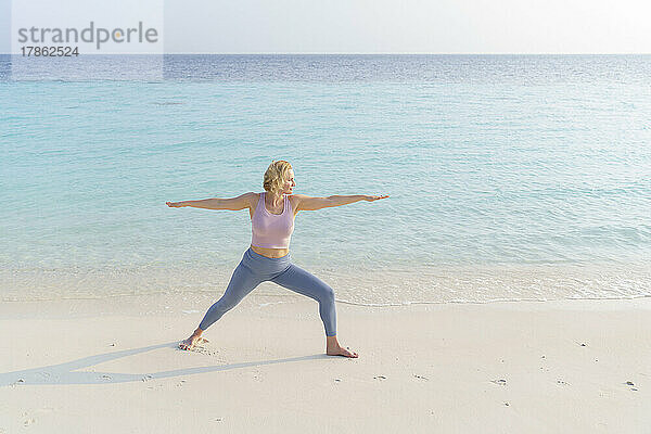 Eine Frau am Strand macht Sport  Yoga.