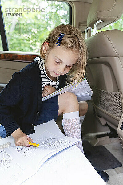 Ein Schulmädchen macht ihre Hausaufgaben auf dem Rücksitz eines Autos.