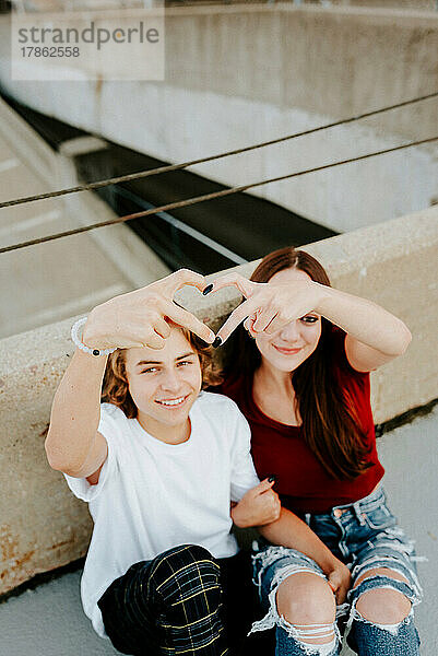 Freund und Freundin sitzen auf dem Dach und machen ein Herzsymbol
