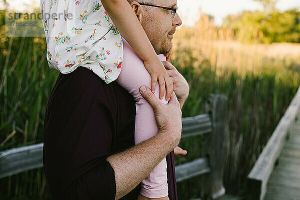 Vater lässt Tochter im goldenen Licht auf Schultern reiten