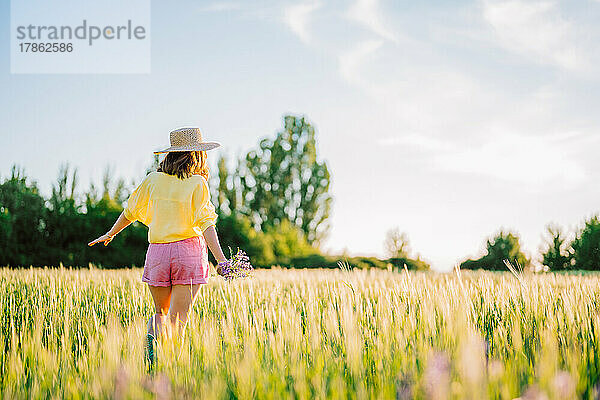 Hübsche Landfrau mit Strohhut  die im Weizenfeld spaziert.