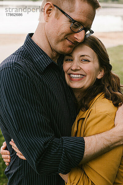 Erwachsenes Ehepaar umarmt und lächelt am Seeufer