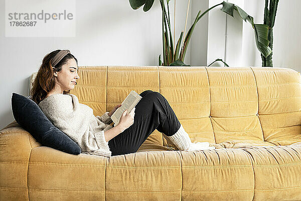 Schöne lächelnde Frau  die ein Buch liest und auf dem Sofa liegt