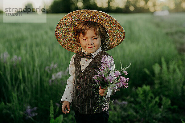 Niedlicher kleiner Junge im festlichen Kostüm mit Blumenstrauß auf offener Fläche