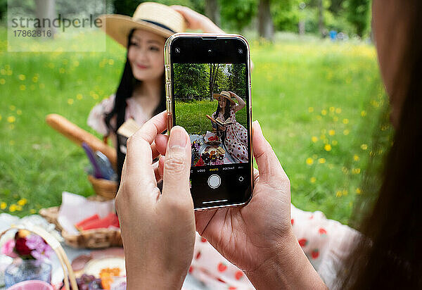 Frau fotografiert ihre Freundin mit einem Mobiltelefon
