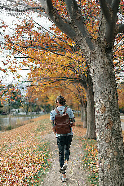 Mann geht im Herbst den Weg entlang und trägt einen minimalen Rucksack