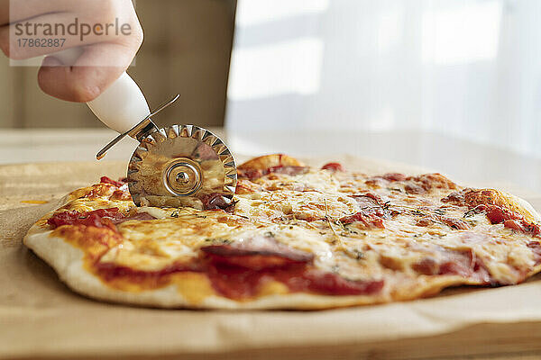Eine Hand mit einem Pizzamesser schneidet eine Pizza aus nächster Nähe.