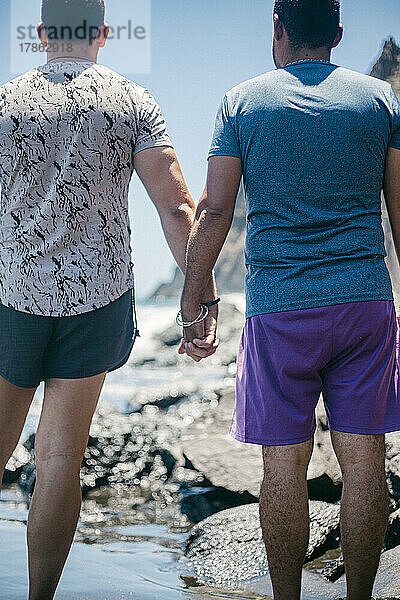Mann mit seinem Freund Händchen haltend am Strand an einem sonnigen Tag