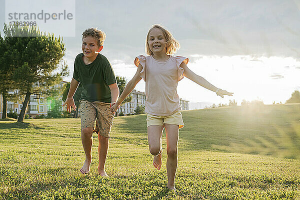 Bruder und Schwester laufen bei Sonnenuntergang im Gras.