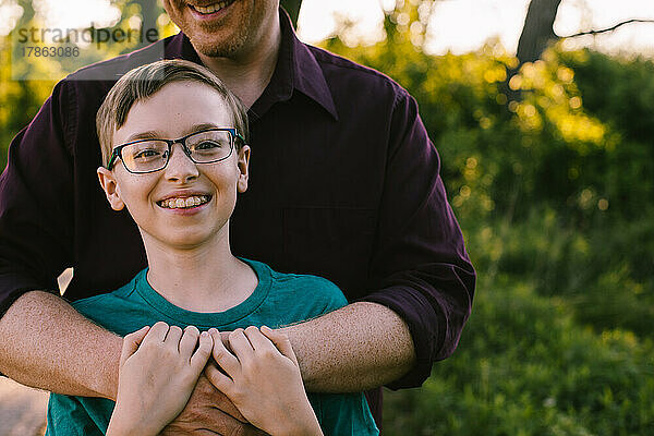 Ein jugendlicher Junge mit Brille lächelt glücklich  während Papa ihn umarmt