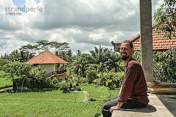 Ein Mann sitzt in einem unfertigen Haus mit Blick auf die Reisfelder