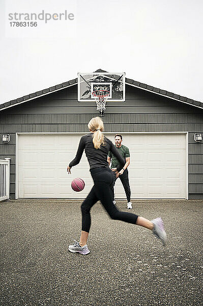 Vater und Tochter im Teenageralter arbeiten in der Einfahrt an Basketballfähigkeiten