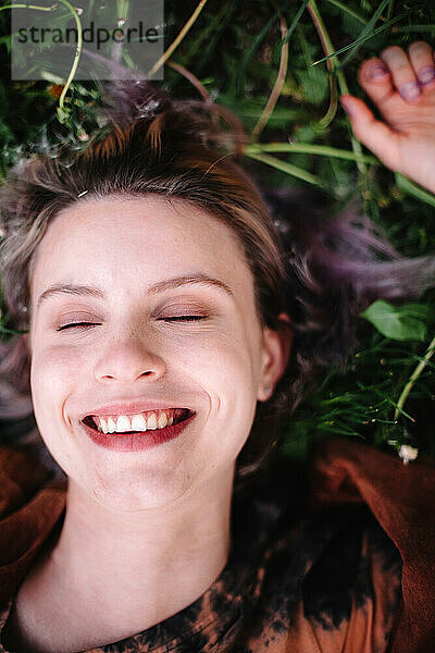 Porträt einer glücklichen jungen Frau  die im Frühling auf Gras liegt