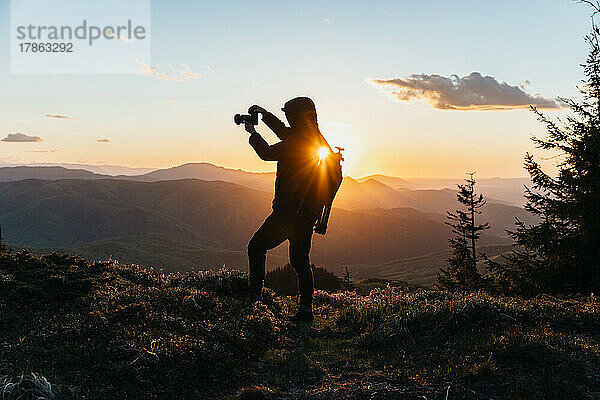 Silhouette eines Mannes mit Kamera bei Sonnenuntergang auf dem Berg