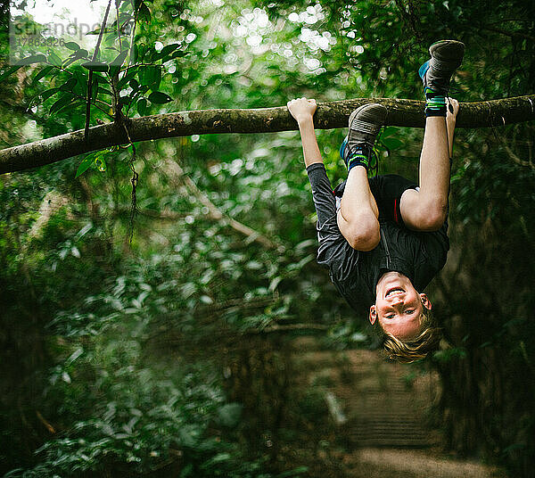 Tween-Junge klettert mit einem Lächeln vom Ast im Wald auf einen Baum