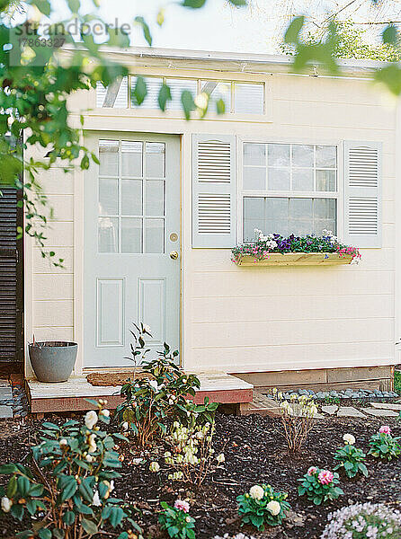 Elfenbeinfarbener Schuppen mit hellblauer Tür und Fensterläden und Blumen