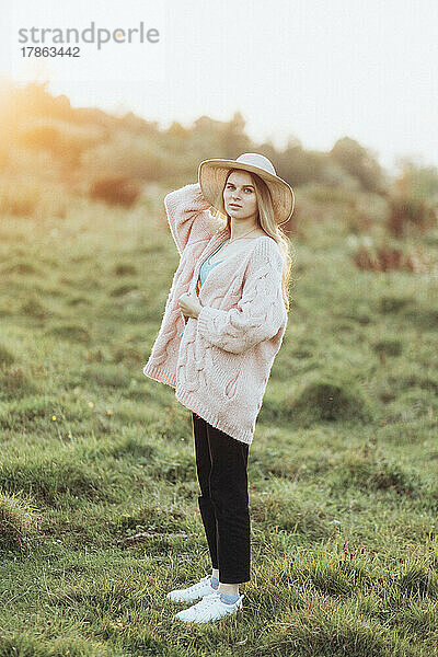 Frau in Jacke und Hut genießt allein den Sonnenuntergang