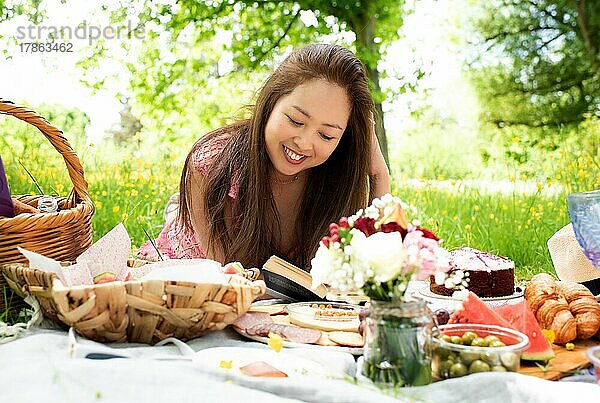 Schöne asiatische Frau liest ein Buch  während sie im Sommer ein Picknick macht