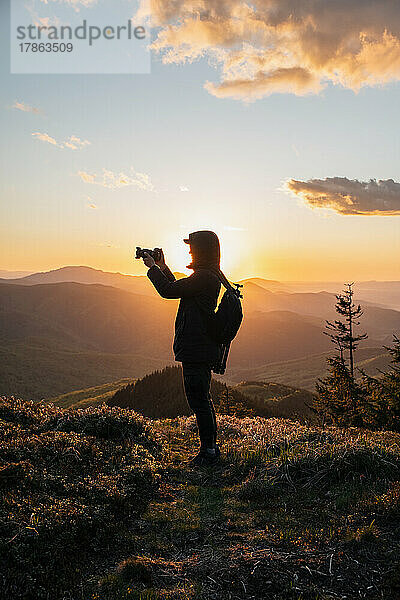 Silhouette eines Mannes mit Kamera bei Sonnenuntergang auf dem Berg